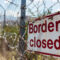 Grungy border closed warning sign on fence with barbed wire with copy space for text. Concept of illegal immigration control and security