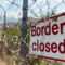 Grungy border closed warning sign on fence with barbed wire with copy space for text. Concept of illegal immigration control and security