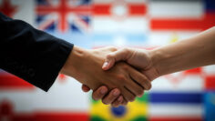 Business handshake with diverse international flags creating diplomatic partnership background. Global cooperation and multicultural relations concept