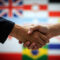 Business handshake with diverse international flags creating diplomatic partnership background. Global cooperation and multicultural relations concept