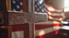 Wooden cross with American flag in soft church lighting.