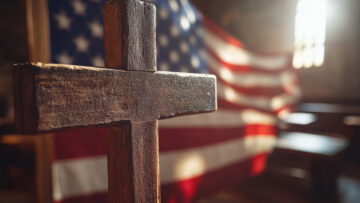 Wooden cross with American flag in soft church lighting.