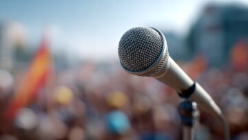 Conditioned microphone standing ready near speaker addressing protesting crowd during immigration raid demonstration in urban setting