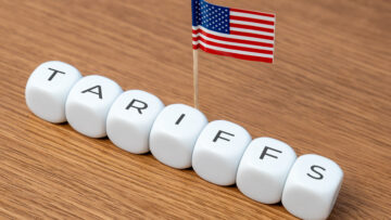 Cubes spelling “TARIFFS” are arranged in a line with a small American flag. Concept of tariffs, particularly in relation to the United States.