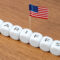 Cubes spelling “TARIFFS” are arranged in a line with a small American flag. Concept of tariffs, particularly in relation to the United States.