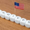 Cubes spelling “TARIFFS” are arranged in a line with a small American flag. Concept of tariffs, particularly in relation to the United States.