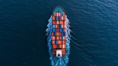 Wide aerial drone shot of container ship complying with IMO Push Green Shipping regulations sailing with zero visible emissions.