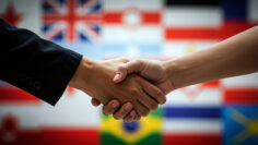 Business handshake with diverse international flags creating diplomatic partnership background. Global cooperation and multicultural relations concept