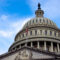 low angle view of American flag on United States Capitol building Washington DC with marble dome and blue sky in background