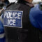 Ice Police Agent – officer of Immigration and Customs Enforcement. Close-up of POLICE ICE marking on the back of a stab proof vest worn by a trio of police officers at the scene of immigrant incident.