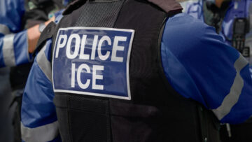 Ice Police Agent – officer of Immigration and Customs Enforcement. Close-up of POLICE ICE marking on the back of a stab proof vest worn by a trio of police officers at the scene of immigrant incident.