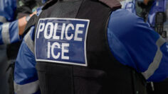 Ice Police Agent – officer of Immigration and Customs Enforcement. Close-up of POLICE ICE marking on the back of a stab proof vest worn by a trio of police officers at the scene of immigrant incident.