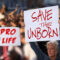 Protesters holding signs Save the unborn, Pro Life. People with placards against abortion rights at protest rally demonstration. Concept image.
