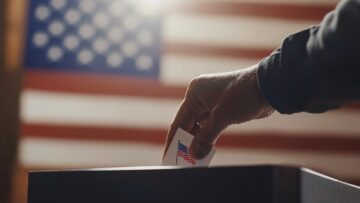 A close-up of a hand placing a ballot into a voting box for the 2024 U.S. elections,