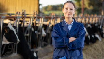 Smiling woman farmer posing in cowshed near stall with cows