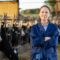 Smiling woman farmer posing in cowshed near stall with cows