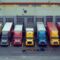 Fleet of colorful semi trucks are parked in front of loading docks at a large distribution warehouse building waiting to be unloaded