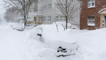 Heavy snow blankets a quiet residential street with cars buried deep after a major Boston blizzard in Brighton, Massachusetts
