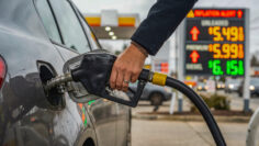 close up of a person refueling a car at a gas station with high fuel prices and an inflation alert displayed on the digital sign in the background, representing rising costs and economic crisis