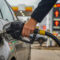close up of a person refueling a car at a gas station with high fuel prices and an inflation alert displayed on the digital sign in the background, representing rising costs and economic crisis